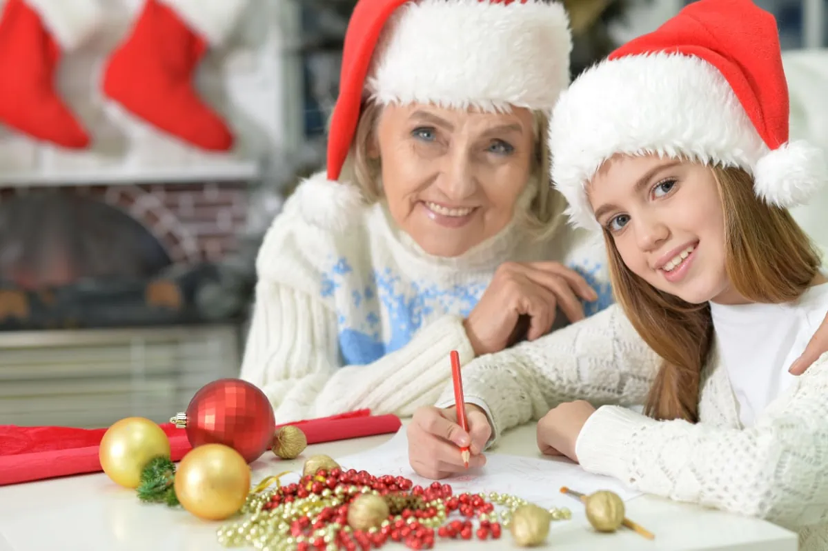 A woman and a girl wearing santa hats writing on a piece of paper.