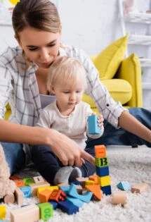 Woman and toddler playing with building blocks on the floor.