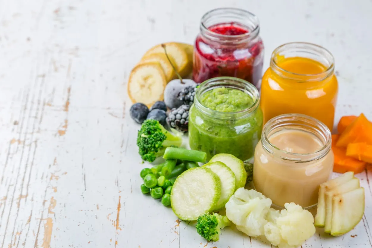 Assorted fruits and vegetables in jars on a wooden table.
