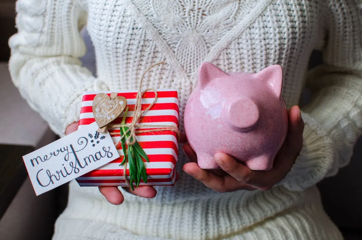 A woman, part of the working poor demographic, holding a piggy bank and a christmas gift.