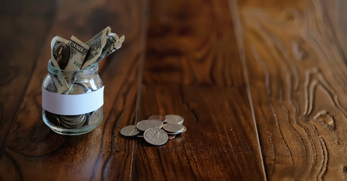 A glass jar filled with money on a wooden table, representing the struggles of the working poor.